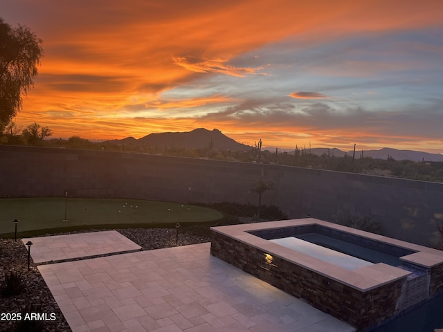 8396 E Granite Pass Rd, Scottsdale, AZ 85266 - patio terrace at dusk with a putting area, a patio area, a mountain view, an in-ground hot tub, and a fenced backyard
