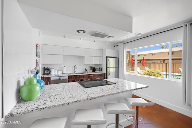 kitchen featuring appliances with stainless steel finishes, a kitchen breakfast bar, a sink, white cabinetry, and modern cabinets