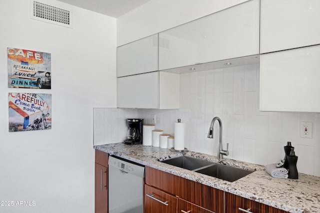 kitchen featuring white dishwasher, a sink, decorative backsplash, and white cabinetry