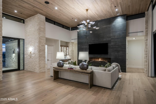 living room featuring a towering ceiling, a fireplace, wooden ceiling, and light wood-type flooring