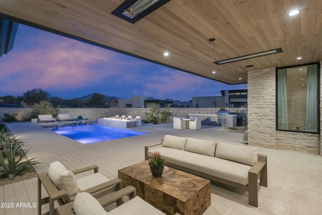 pool at dusk with an outdoor kitchen, an outdoor hangout area, pool water feature, and a patio area