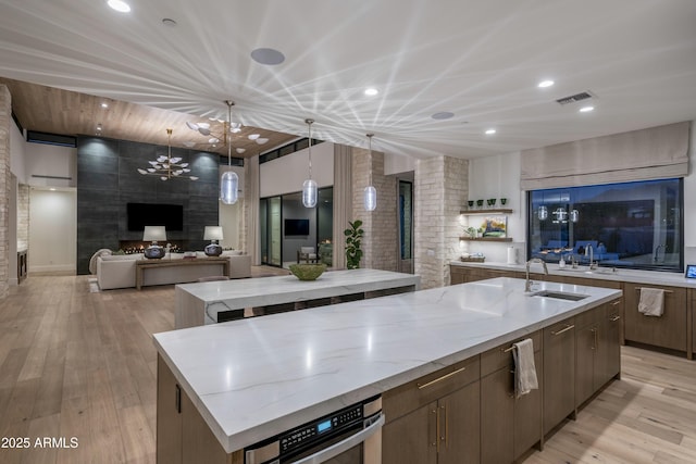 kitchen with a spacious island, hanging light fixtures, sink, and light hardwood / wood-style flooring