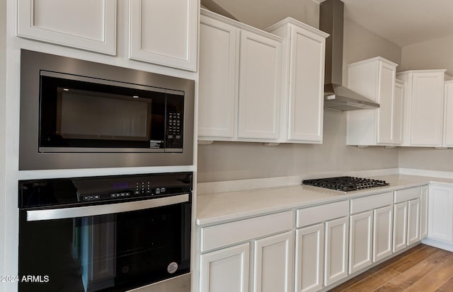 kitchen with white cabinets, wall chimney exhaust hood, light wood-type flooring, and stainless steel appliances