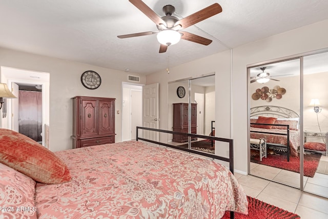 bedroom with light tile patterned flooring, two closets, ceiling fan, and a textured ceiling