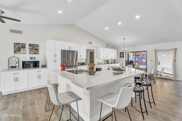 kitchen with white cabinets, hanging light fixtures, a large island, light countertops, and black appliances