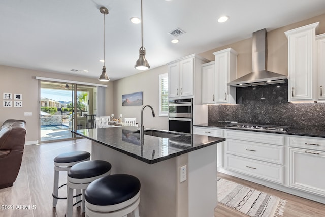 kitchen featuring appliances with stainless steel finishes, wall chimney exhaust hood, sink, pendant lighting, and an island with sink