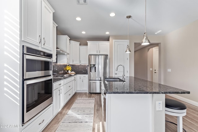 kitchen with sink, stainless steel appliances, a kitchen island with sink, white cabinets, and light wood-type flooring