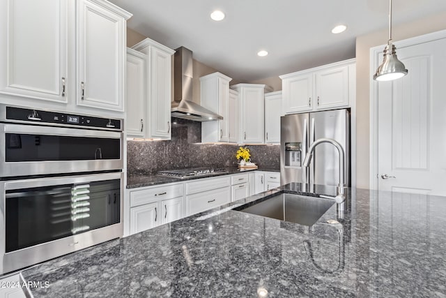 kitchen with white cabinets, wall chimney exhaust hood, stainless steel appliances, and hanging light fixtures