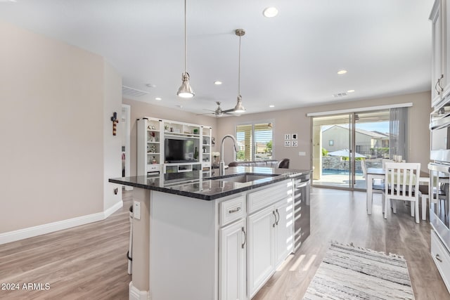 kitchen with dark stone countertops, white cabinetry, a center island with sink, and ceiling fan