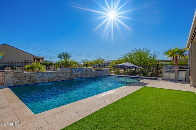 view of pool with a yard, pool water feature, an outdoor kitchen, and a patio area