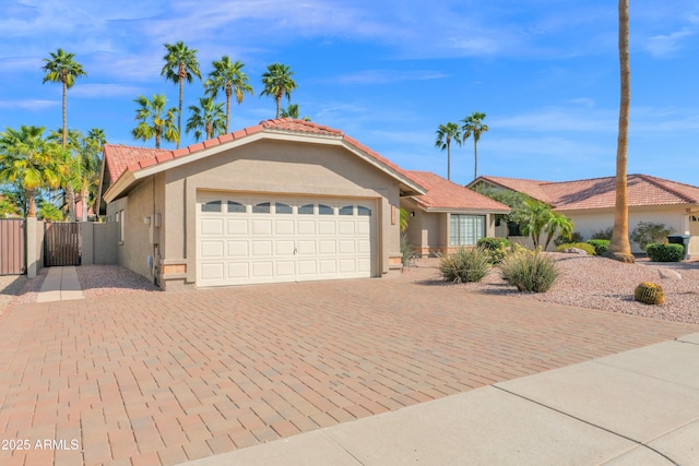 view of front facade with stucco siding, decorative driveway, fence, a garage, and a tiled roof