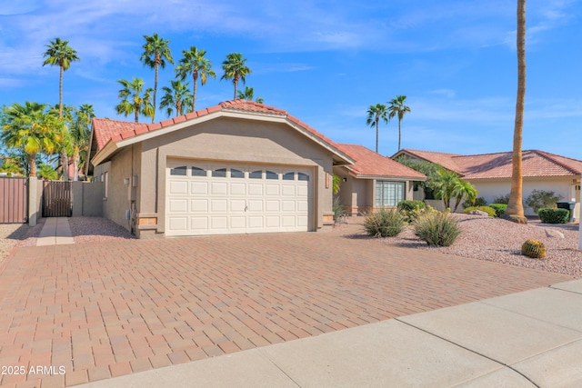 view of front facade with fence, stucco siding, decorative driveway, an attached garage, and a gate