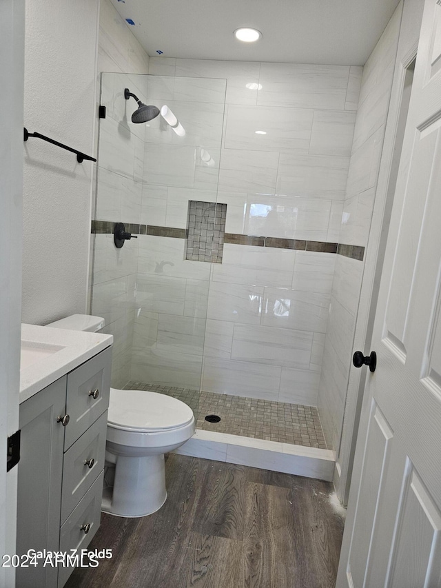 bathroom featuring a tile shower, toilet, vanity, and hardwood / wood-style flooring