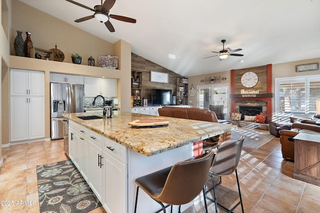 kitchen with a stone fireplace, sink, white cabinetry, light stone counters, and a kitchen island with sink