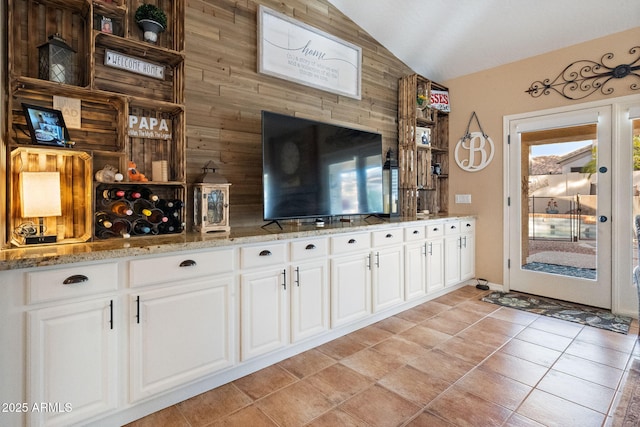 bar featuring light stone countertops, white cabinetry, lofted ceiling, and light tile patterned floors