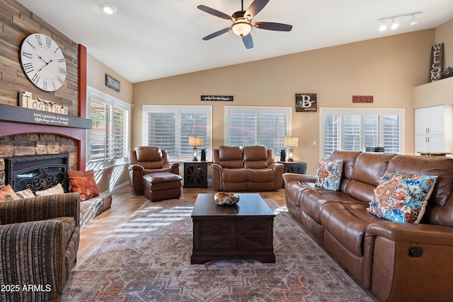 living room featuring vaulted ceiling, a stone fireplace, and ceiling fan