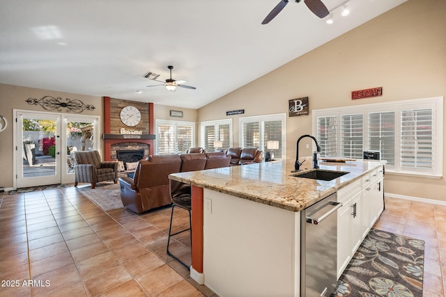 kitchen with a fireplace, white cabinetry, sink, light stone countertops, and a center island with sink