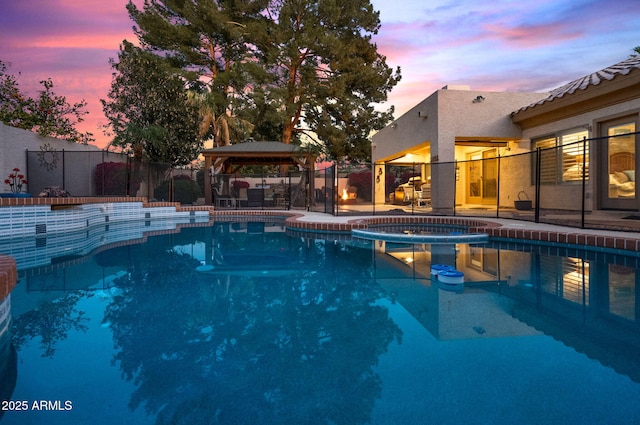 pool at dusk with a gazebo and an in ground hot tub