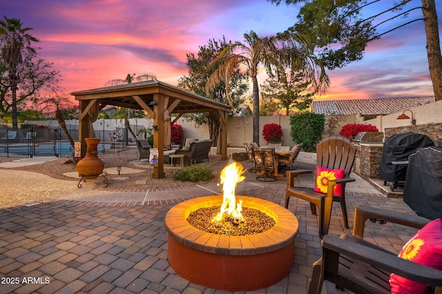 patio terrace at dusk with a gazebo, area for grilling, and an outdoor fire pit