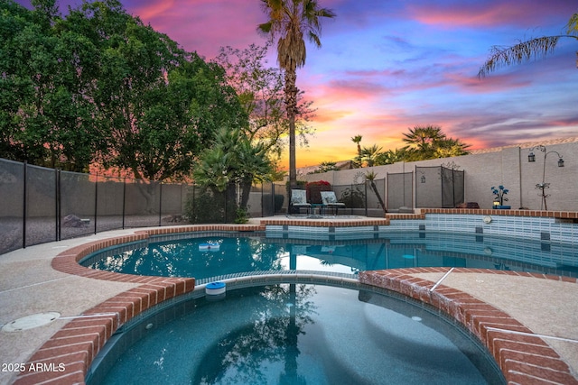 pool at dusk with an in ground hot tub