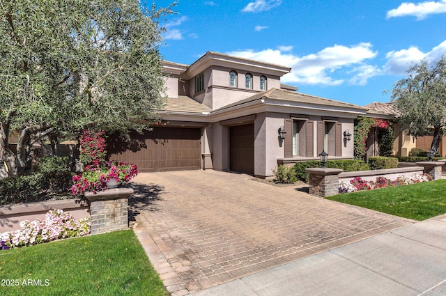 prairie-style house featuring a front lawn, decorative driveway, an attached garage, and stucco siding