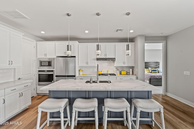 kitchen featuring pendant lighting, appliances with stainless steel finishes, an island with sink, and white cabinets