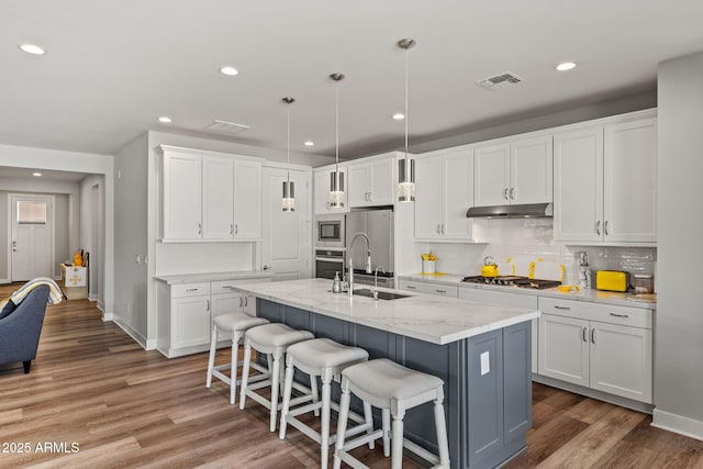 kitchen with white cabinetry, a kitchen bar, hanging light fixtures, stainless steel appliances, and a center island with sink