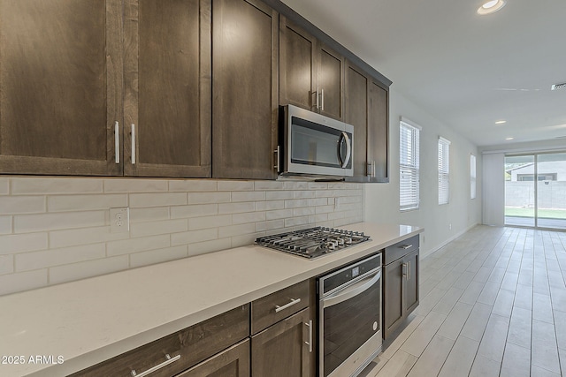 kitchen featuring stainless steel appliances, backsplash, baseboards, dark brown cabinets, and recessed lighting