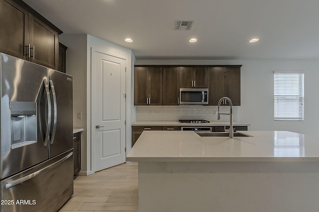 kitchen featuring appliances with stainless steel finishes, a sink, decorative backsplash, dark brown cabinetry, and recessed lighting