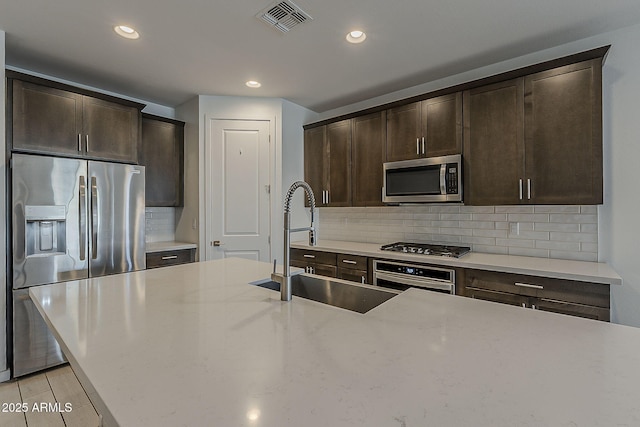 kitchen with appliances with stainless steel finishes, a sink, dark brown cabinets, tasteful backsplash, and recessed lighting