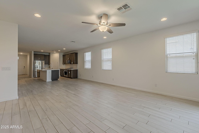 unfurnished living room featuring ceiling fan, baseboards, a sink, recessed lighting, and light wood-style floors