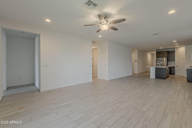 unfurnished living room featuring a ceiling fan, recessed lighting, light wood-style floors, baseboards, and a sink