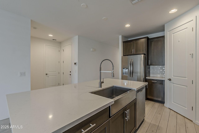 kitchen with stainless steel appliances, a sink, dark brown cabinets, backsplash, and recessed lighting