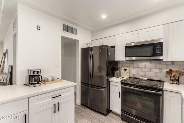 kitchen featuring stainless steel appliances, white cabinetry, backsplash, and light wood-type flooring