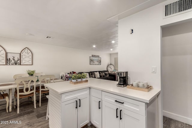 kitchen with kitchen peninsula, hardwood / wood-style floors, and white cabinets