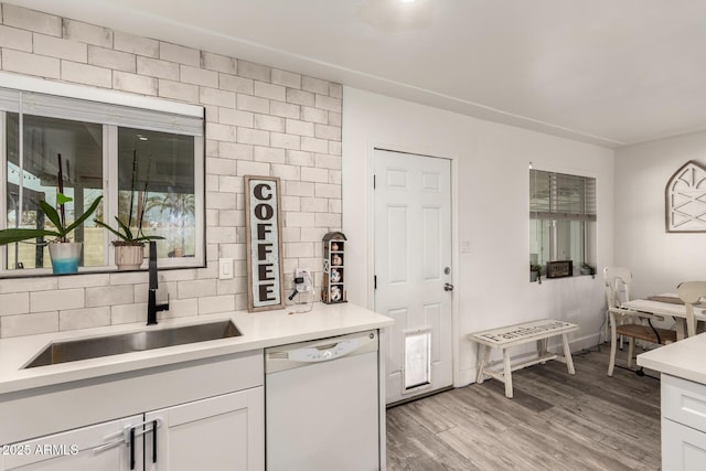 kitchen with sink, white dishwasher, white cabinets, light hardwood / wood-style floors, and backsplash