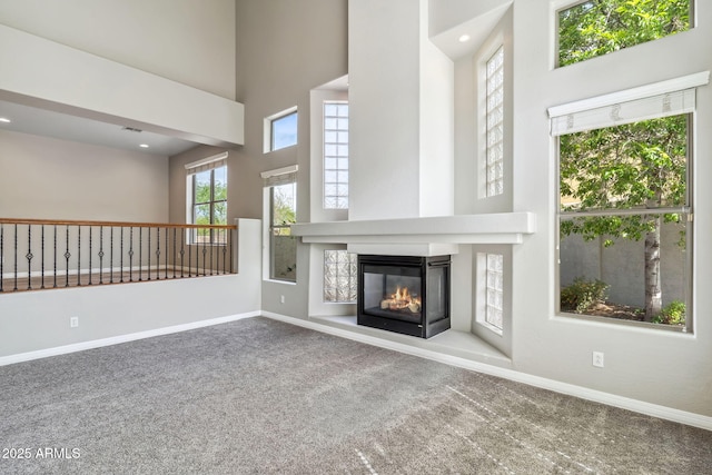unfurnished living room featuring a multi sided fireplace, baseboards, a high ceiling, and carpet floors
