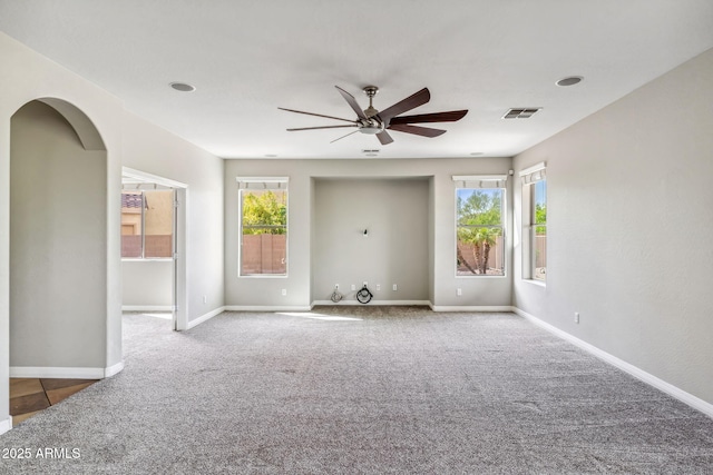 carpeted empty room featuring baseboards, arched walkways, visible vents, and a ceiling fan