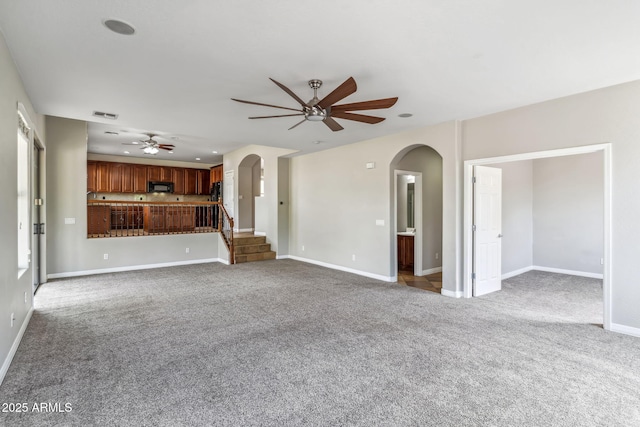 unfurnished living room with a ceiling fan, carpet floors, arched walkways, and visible vents