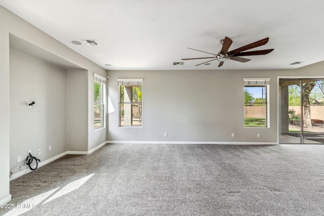 spare room featuring a wealth of natural light, visible vents, carpet flooring, and a ceiling fan