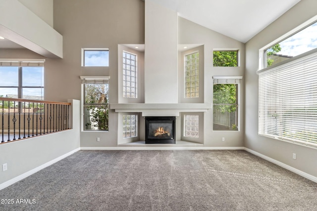 unfurnished living room featuring baseboards, carpet flooring, high vaulted ceiling, and a glass covered fireplace