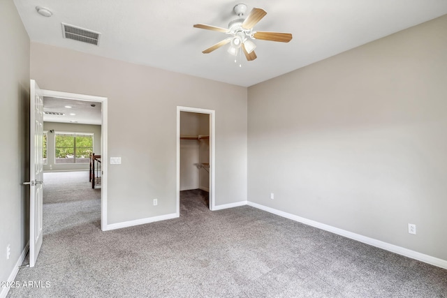 unfurnished bedroom featuring visible vents, baseboards, a ceiling fan, carpet floors, and a walk in closet