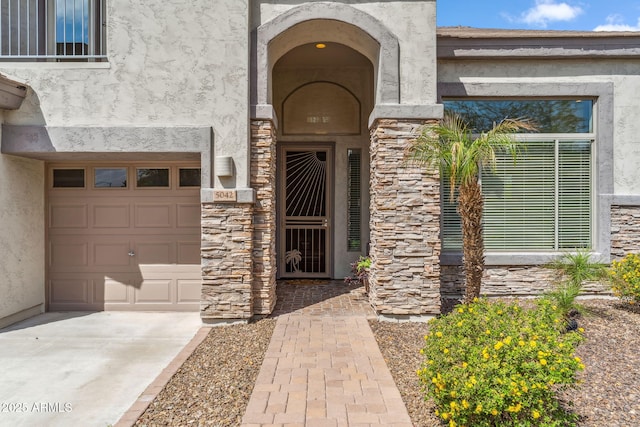 view of exterior entry with stucco siding, an attached garage, and stone siding