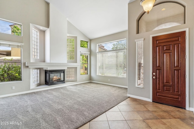 carpeted entryway featuring baseboards, high vaulted ceiling, tile patterned flooring, and a glass covered fireplace