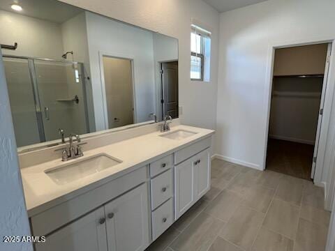 bathroom featuring a shower stall, double vanity, a spacious closet, and baseboards