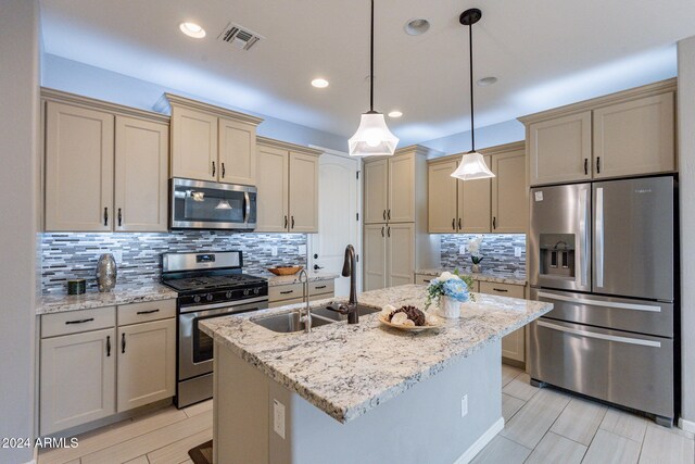 kitchen featuring appliances with stainless steel finishes, decorative light fixtures, light stone counters, and an island with sink