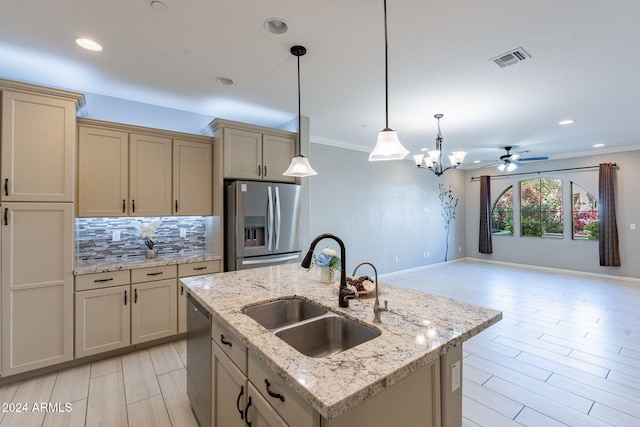 kitchen with cream cabinetry, hanging light fixtures, stainless steel appliances, a center island with sink, and sink