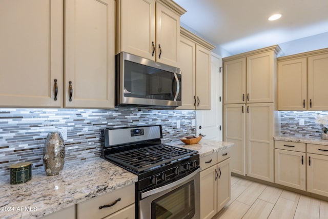 kitchen with decorative backsplash, light stone counters, stainless steel appliances, and cream cabinets