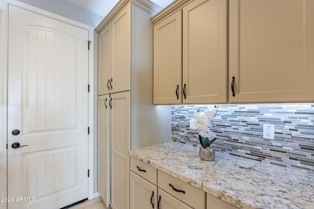 kitchen featuring cream cabinetry, light stone counters, and backsplash