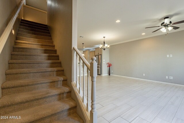 stairs featuring crown molding and ceiling fan with notable chandelier